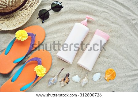 Bottle of lotion and cream with accessories on sand beach.