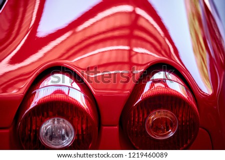 Close up of tail light detail of modern luxury sportscar with reflection on red paint after wash & wax. Rear view of supercar break lights. Concept of car detailing and paint protection background.