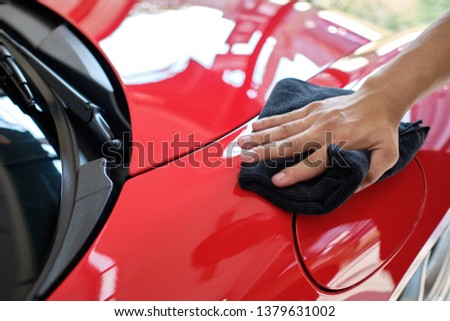 Man's hand cleaning car and drying vehicle with microfiber cloth. Hand wipe down paint surface of shiny red sport sedan after polishing and ceramic coating. Car detailing and car wash concept.