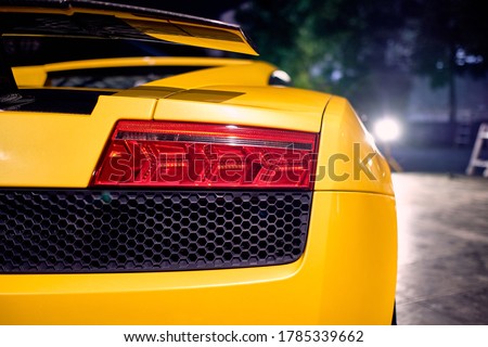 Close up of taillight detail of modern luxury sportscar with reflection on yellow paint after wash & wax. Rear view of supercar. Concept of car detailing and paint protection background. Night shot.