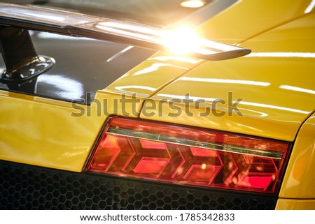 Close up of taillight of modern luxury sportscar with sunlight reflection on spoiler. Shiny yellow paint after wash & wax. Rear view of supercar. Concept of car detail and paint protection background.