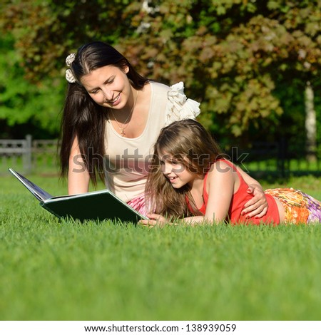 Mom and daughter reading a book in a beautiful park