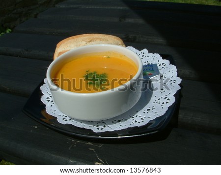 Bowl of Vegetable soup with bread roll on black saucer.