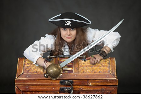 Female sexy pirate with chest of treasure and saber on black background.