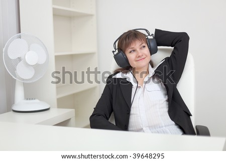 The woman sits in an armchair and listens to music in the big ear-phones