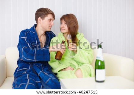 The young pair at home on a divan with beer and wine