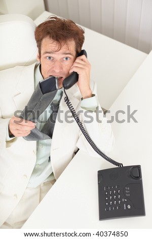 The young businessman speaks on the phone, worries and bites a tie