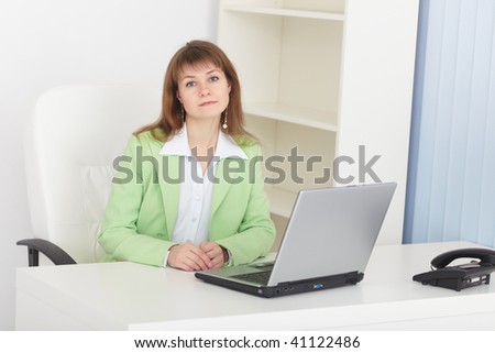The businesswoman sits at a table at light office with the laptop