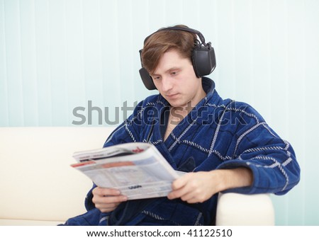 The person in the big ear-phones sits on a sofa reads the newspaper