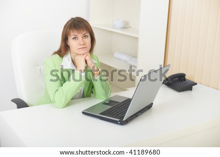 The young woman with the laptop sits at a table at light office