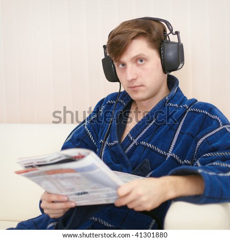 Person in the big ear-phones sits on a sofa reads the newspaper