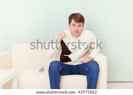 The young man sits on a sofa and watches football on TV