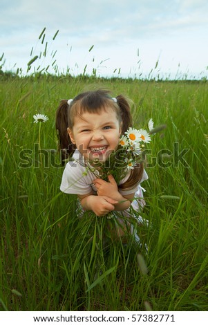 The cheerful child embraces wild flowers in the field