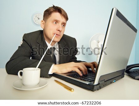 The amusing businessman drinks coffee through a straw without distracting from work in the Internet