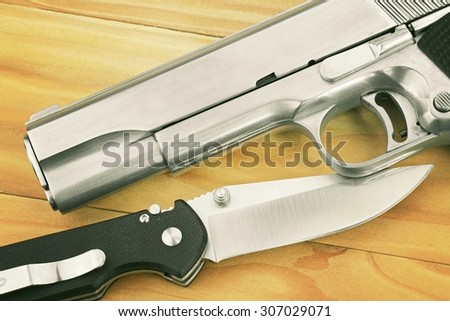 Semi-automatic handgun and tactical knife on wooden background, .45 pistol. (Vintage Style Color)