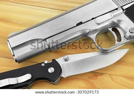 Semi-automatic handgun and tactical knife on wooden background, .45 pistol.