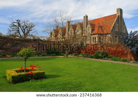a Courtyard with green lawn and red poppy in blossom with Victoria Style house outside the wall of red bricks against blue sky in England, United Kingdom