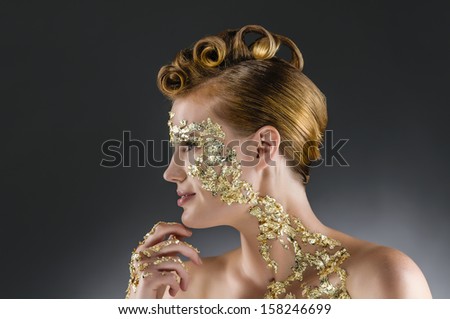 Side portrait of a young woman with an elegant gold leaf make-up and hair styling with an exclusive screwed curls.