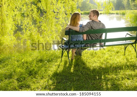 A young couple is romantic in the park on a lake on the go. They sit in the evening light on a park bench and look at a lake.