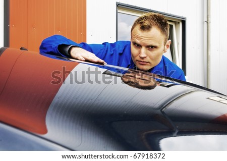 Auto Mechanics sweeps his hand over a car and checked the paint in front of the garage, his face is reflected in the paint