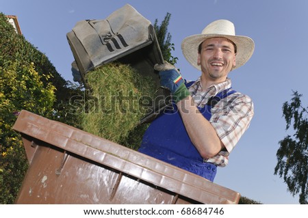 Man with straw hat attacks the organic waste with grass clippings in the garden and laughs at the camera