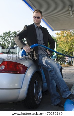 Handsome young man in a dark suit stands at the gas station and fueled his silver sports car