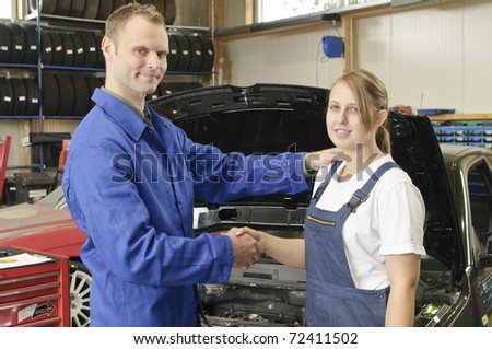 The auto mechanic congratulates its students on passing the exam with flowers in the garage in front of a car