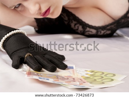Young pretty woman with blonde hair holding a bundle of banknotes seductive in her hand, against a white background.