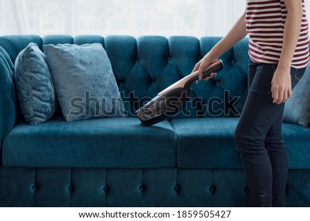 Close up of A woman housewife vacuuming furniture in a house with a hand-held portable vacuum cleaner