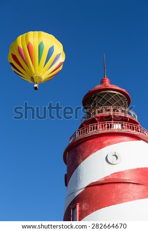 Hot Air Balloon flies over a red and white striped light house.