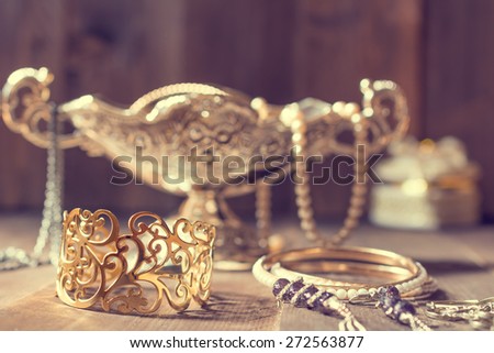 Vintage golden bracelet and silver vase with jewelry on wooden background