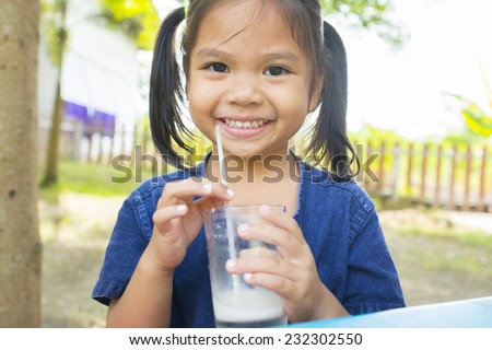 Asia little girl is dipping his tongue in the glass of milk