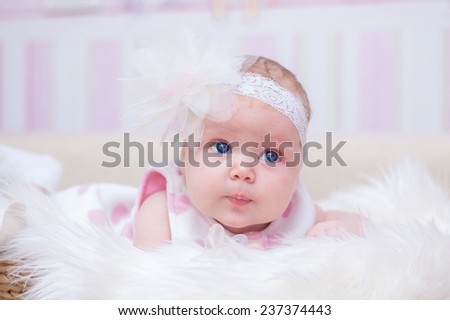 Small  sweet baby girl with white flower headband is lying on the fluffy blanket