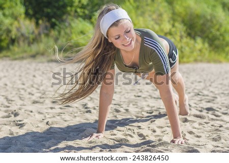 Young pretty girl does push-ups workout on the beach at sunny day