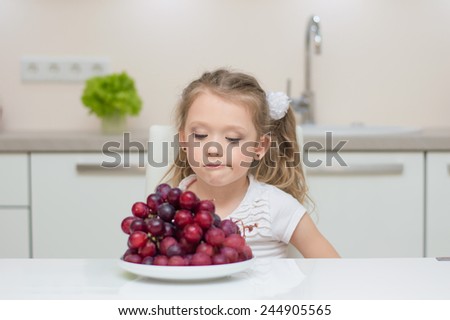Little young beautiful cute sweet pretty girl portrait in the kitchen. Child refuse to eat healthy fresh grapes