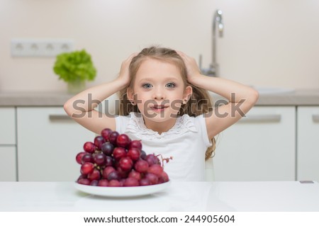 Little young beautiful cute sweet pretty girl portrait in the kitchen. Child refuse to eat healthy fresh grapes