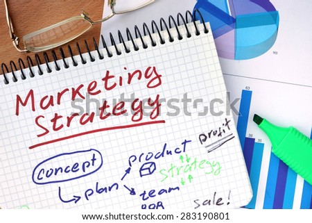 Notepad with  Marketing Strategy concept on a wooden board.