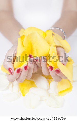 Woman with beautiful manicured fashion nails holding a handful of yelow rose petals