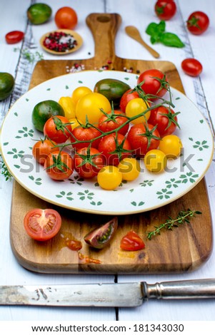 Freshly washed yellow, red, green and black tomatoes, herbs, salt and pepper and a rusty knife on a vintage plate on a wooden cutting board
