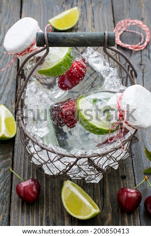 Refreshing lemonade on ice made of lime, mint, thyme and cherry in a vintage basket on a surface of natural dark wood