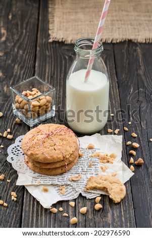 Peanut butter cookies, peanuts and a bottle of milk on a surface of dark natural wood