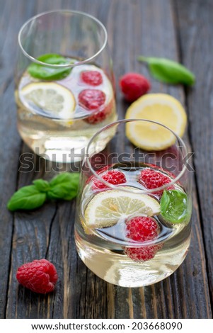 Raspberry basil cocktail with sparkling white wine, slice of lemon, ice cubes  and elderberry syrup on a natural wooden surface
