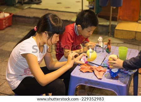 Hanoi, Vietnam - Nov 2, 2014: Children learn to paint plaster figurine by brush and color ink on Ma May street, quarter of Hanoi. Focus on the plaster figurine