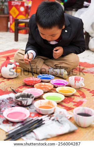 Hanoi, Vietnam - Feb 7, 2015: Schoolboy learn to paint plaster figurine by brush and color ink at Vietnamese lunar new year festival organized at Vinschool, Vinhomes Times City, Minh Khai