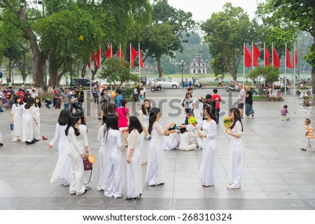 Hanoi, Vietnam - Apr 5, 2015: Group of students in Vietnamese traditional dress Ao Dai taking photos at Ly Thai To park, Dinh Tien Hoang street, by Hoan Kiem lake