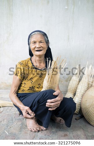Hung Yen, Vietnam - July 26, 2015: Old woman weaves bamboo fish trap at Vietnamese traditional crafts village Thu Sy, Hung Yen province.