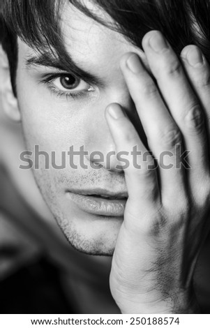 Close up of male face. ?lose half face with his hand. Black and white portrait.