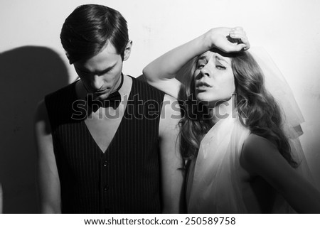 Beautiful wedding couple fool around. Standing beside on white wall background. Black and white portrait