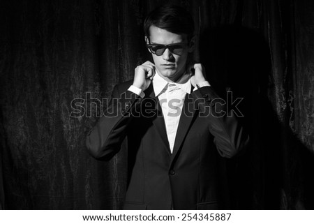 Handsome young man in business suit stay on drapes background.straightens the collar. Black and white portrait.