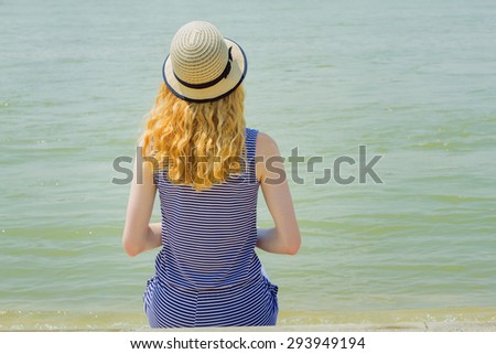Young woman sitting back on beach of river.